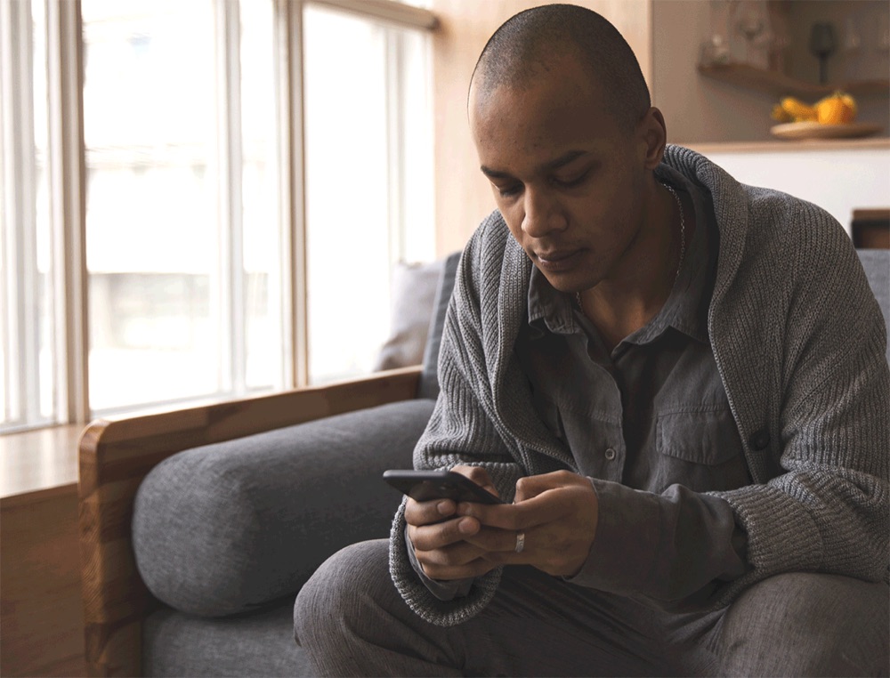A man sitting by a window using his phone.
